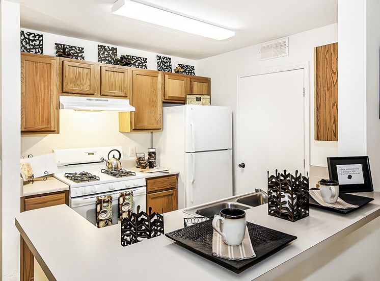Model apartment kitchen with white appliances, brown cabinets, and breakfast bar.